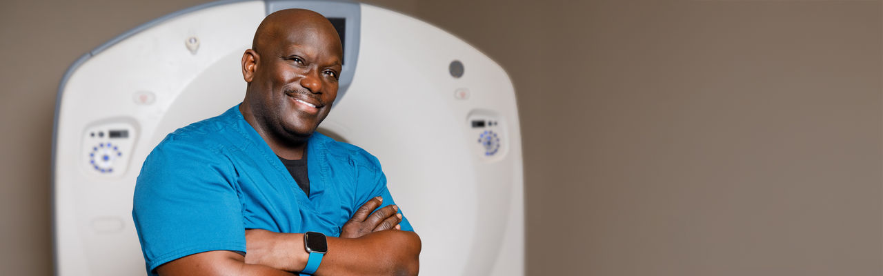 technician in front of CT scanner smiling mobile sized