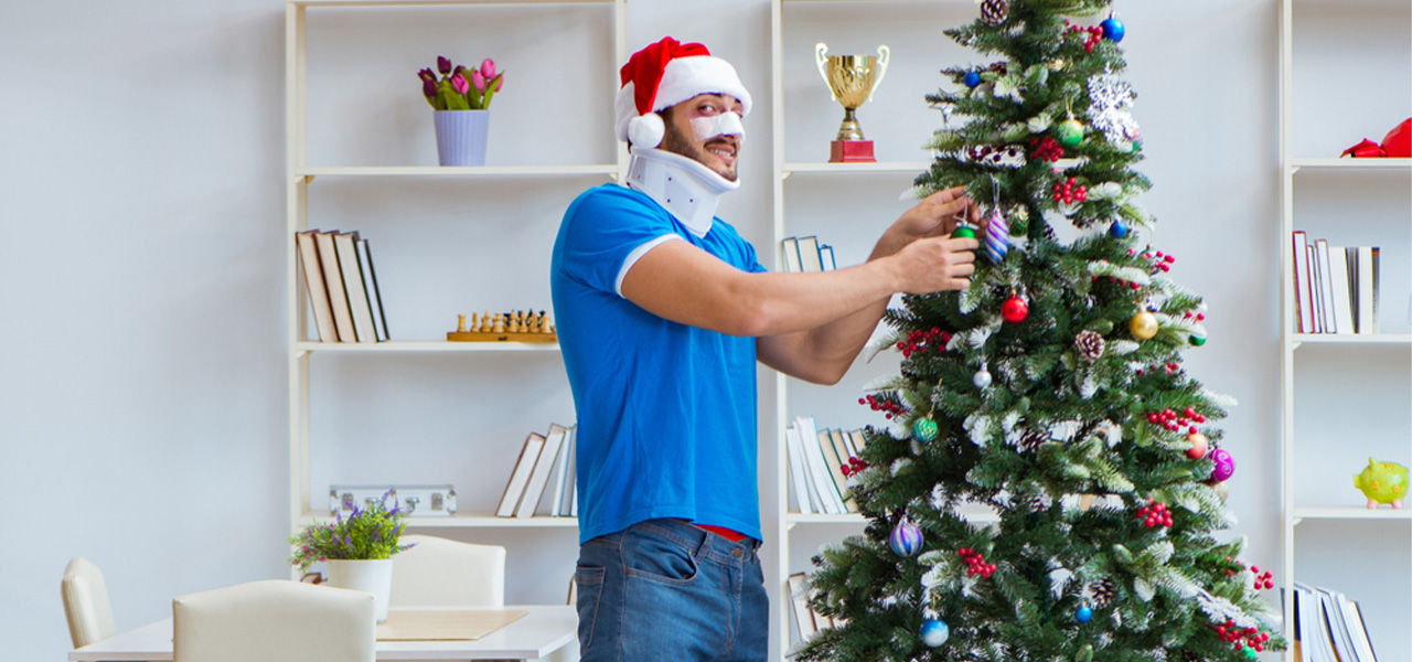 man decorates christmas tree with neck collar on and a broken nose bandage